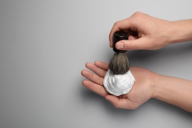 Photo of Man applying shaving foam onto brush on light grey background, top view. Space for text