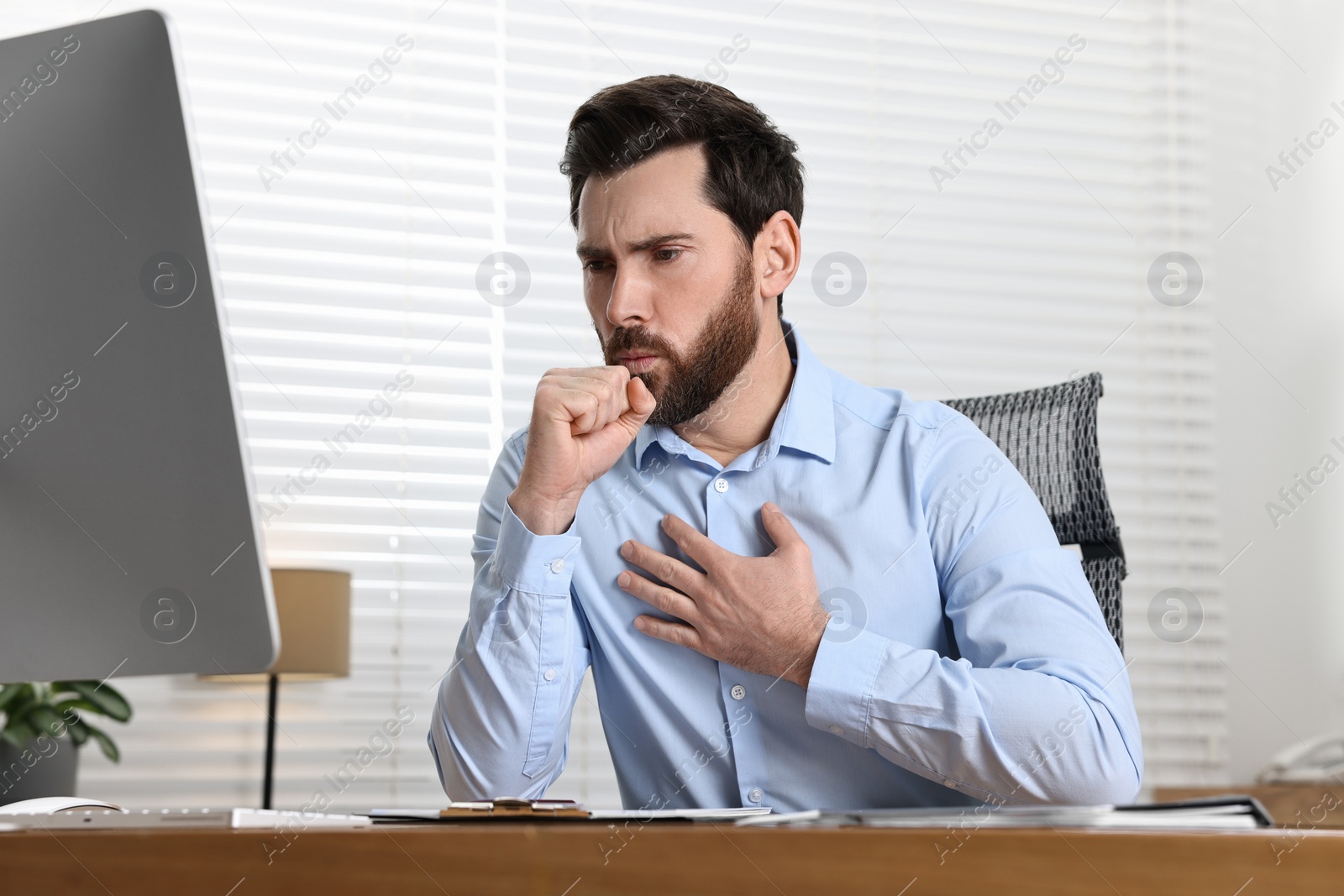 Photo of Sick man coughing at workplace in office. Cold symptoms
