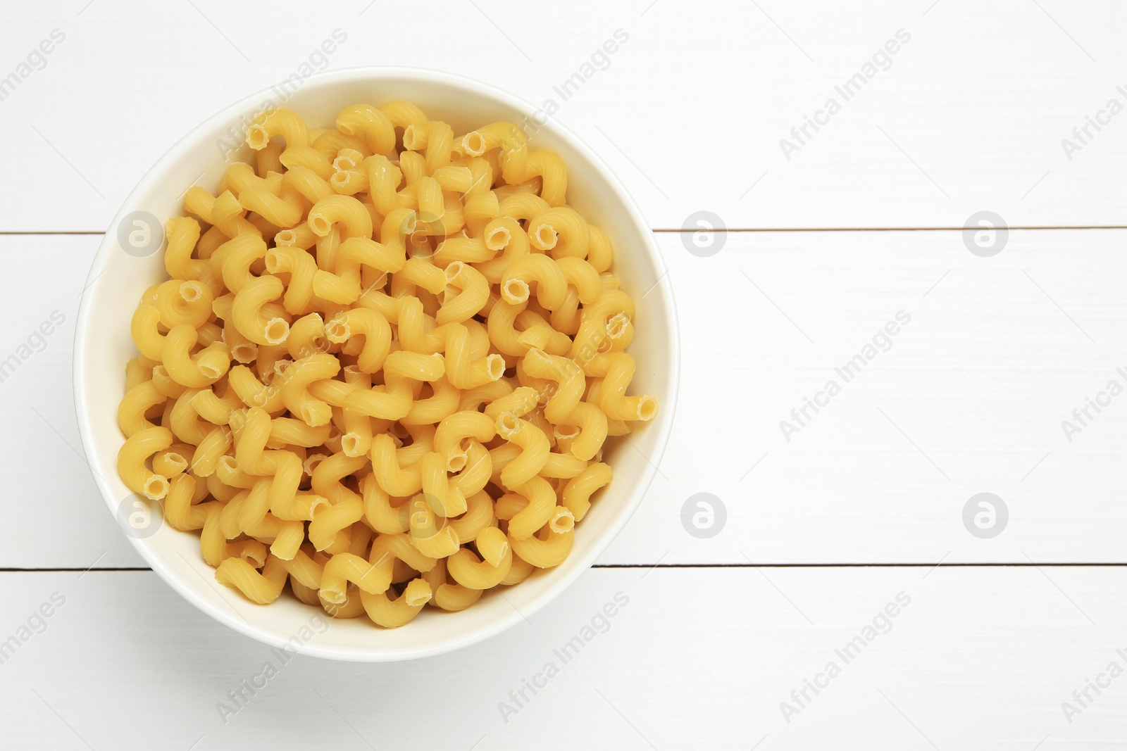 Photo of Raw cavatappi pasta in bowl on white wooden table, top view. Space for text