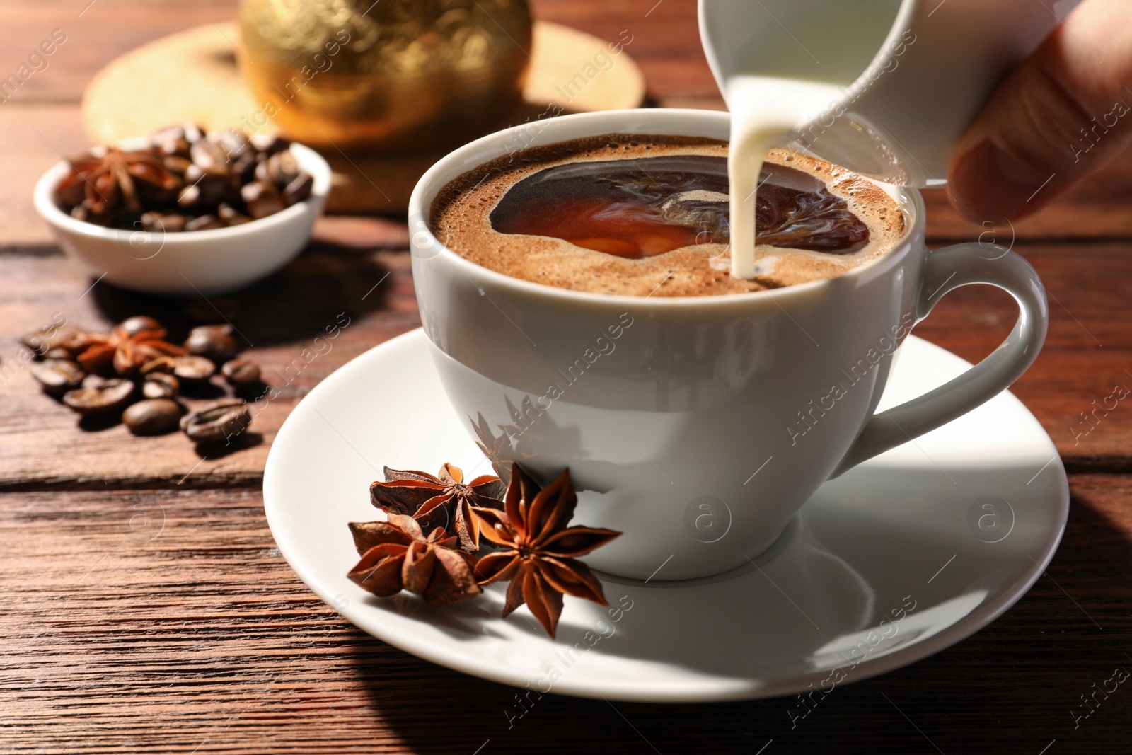 Photo of Woman pouring milk into cup of coffee with anise stars at wooden table