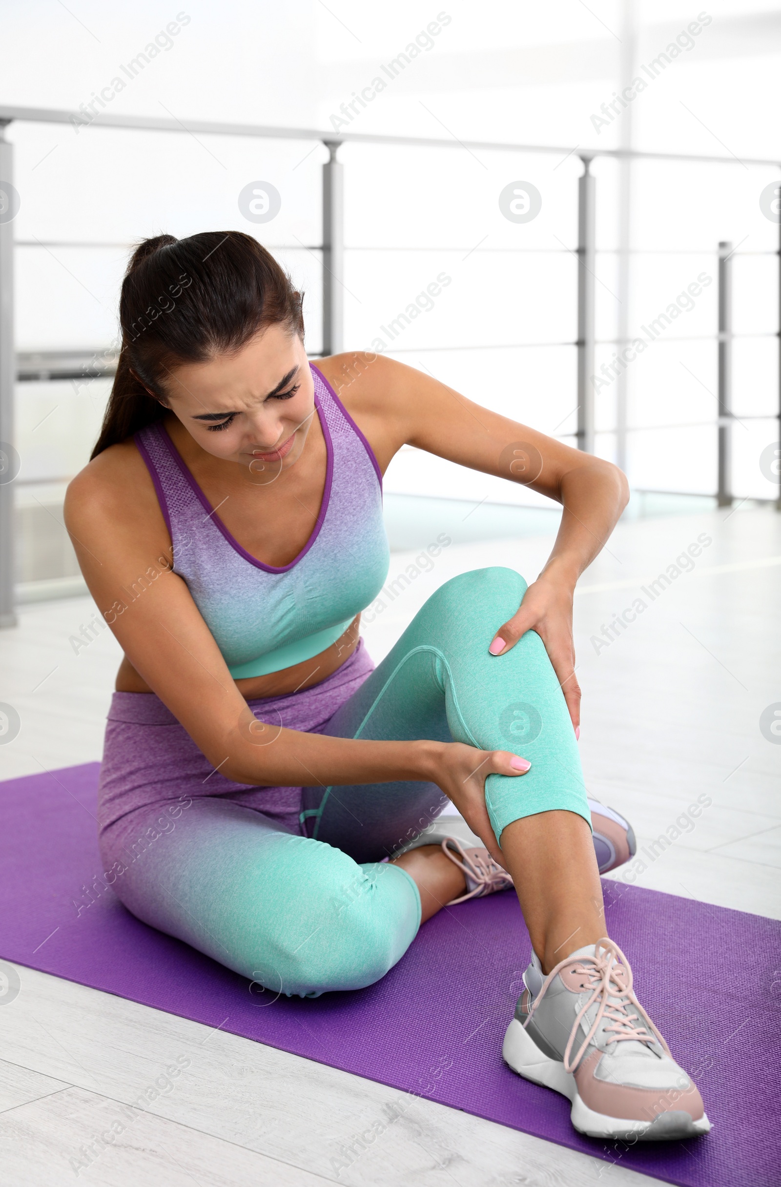 Photo of Young woman in sportswear having knee problems at gym