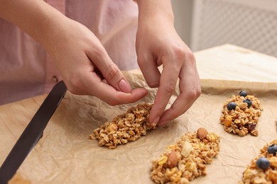 Photo of Making granola bars. Woman putting mixture of oat flakes, dry fruits and other ingredients onto baking tray at table in kitchen, closeup