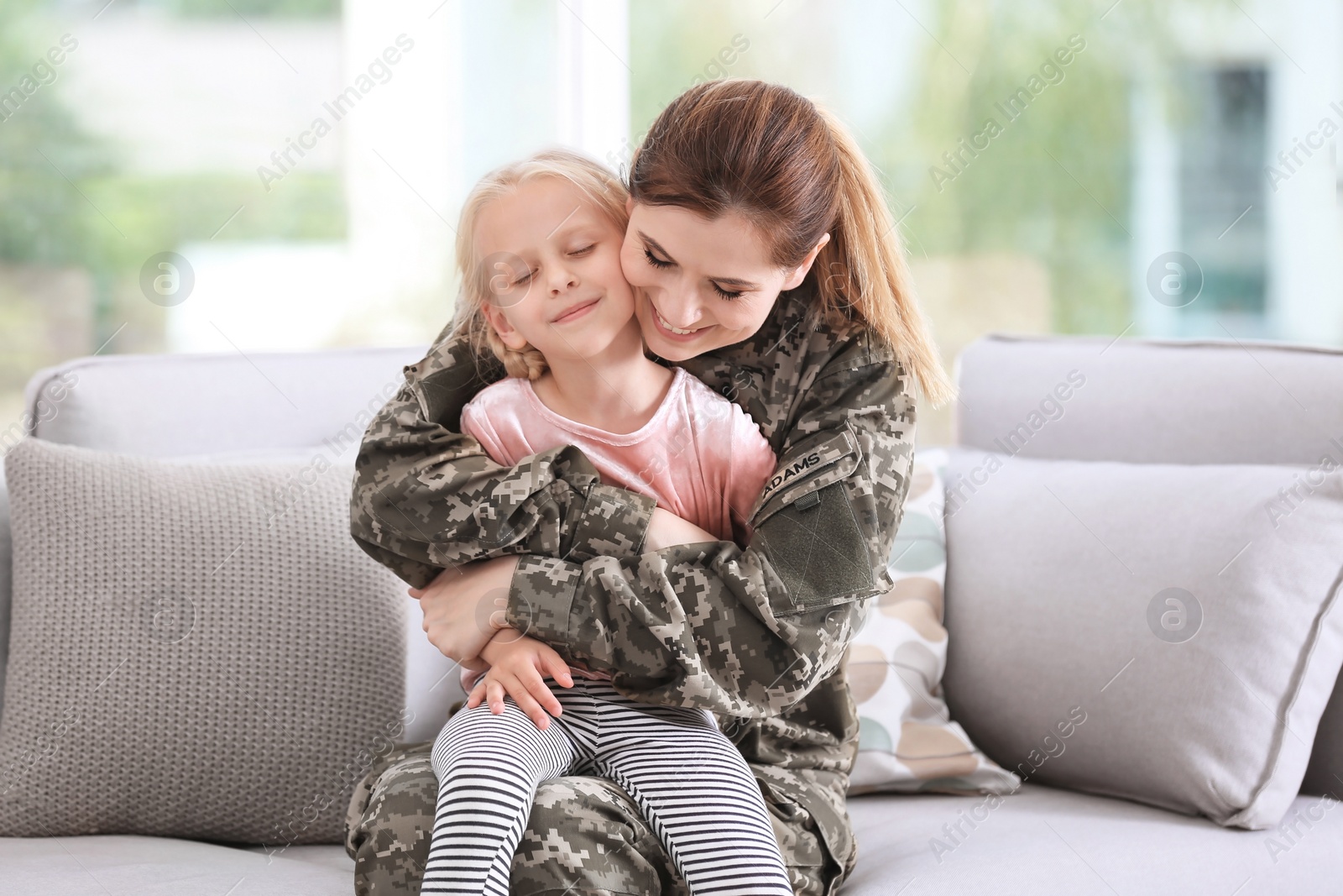 Photo of Woman in military uniform with her little daughter  on sofa at home