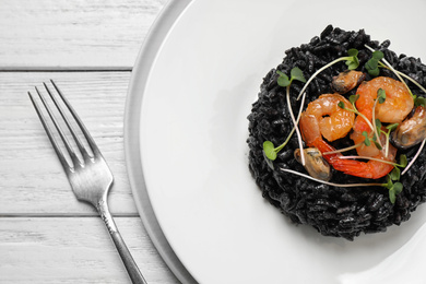 Delicious black risotto with seafood on white wooden table, top view