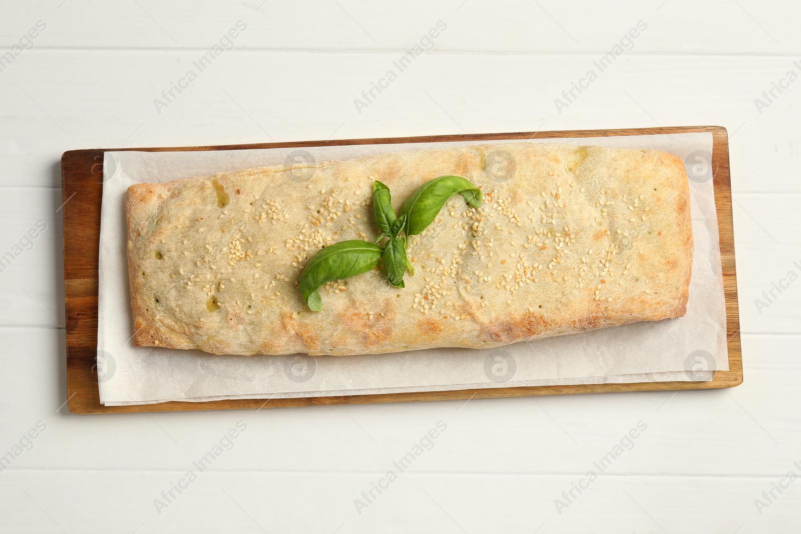 Photo of Delicious strudel with tasty filling and basil on white wooden table, top view