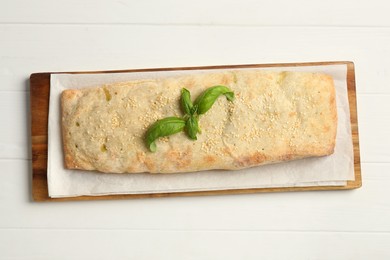 Delicious strudel with tasty filling and basil on white wooden table, top view