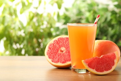 Photo of Glass of delicious grapefruit juice on wooden table against blurred background, space for text