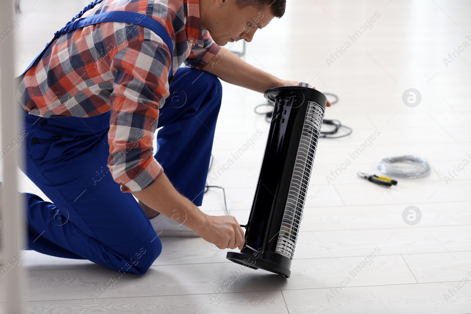 Photo of Professional technician repairing electric halogen heater with screwdriver indoors