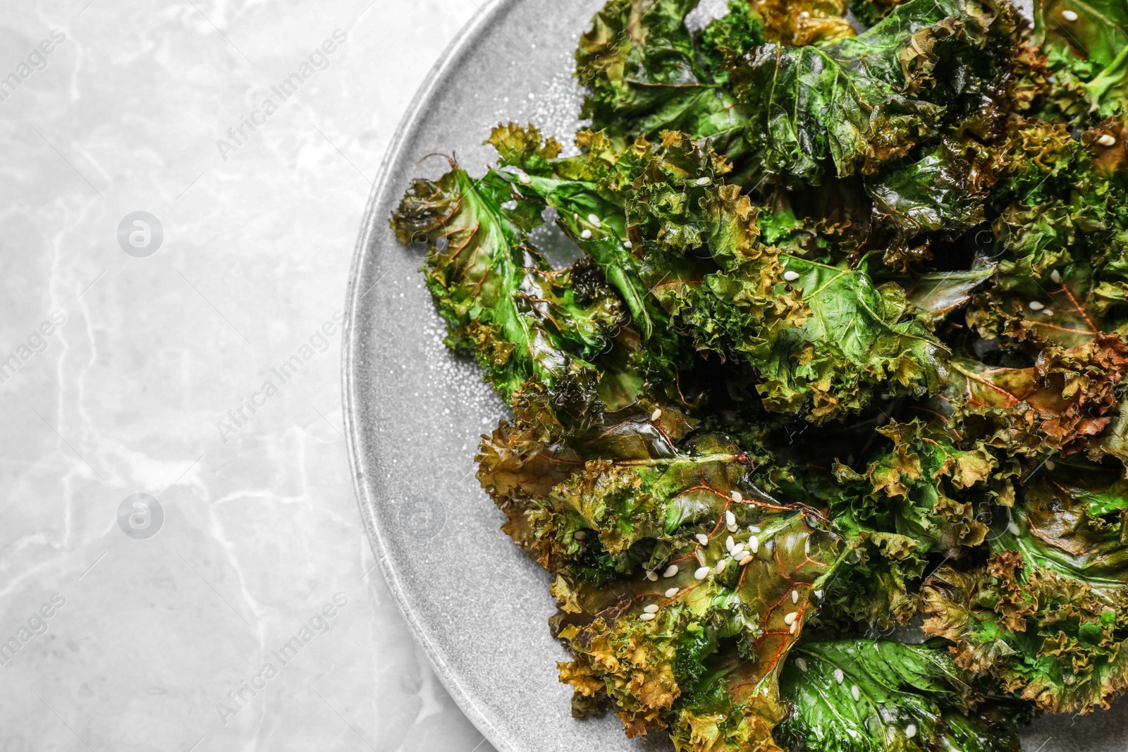 Photo of Tasty baked kale chips on light grey marble table, top view