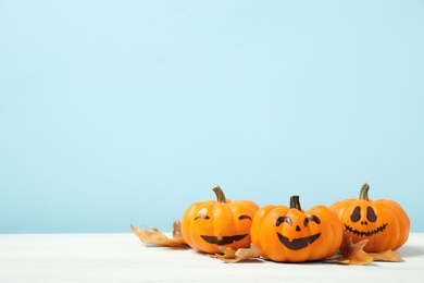 Photo of Pumpkins with scary faces and fallen leaves on white wooden table, space for text. Halloween decor