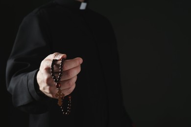 Photo of Priest with rosary beads on dark background, closeup. Space for text