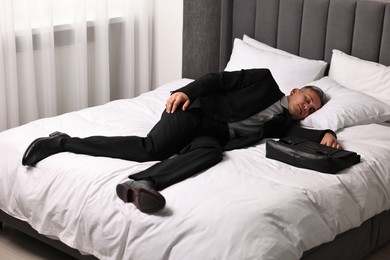 Photo of Businessman with briefcase sleeping on bed indoors
