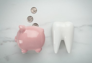 Ceramic model of tooth, piggy bank and coins on white table, flat lay. Expensive treatment