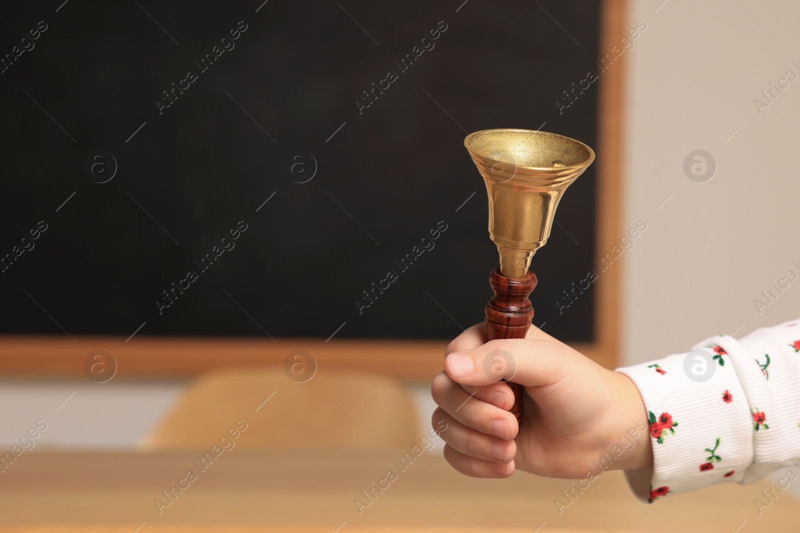 Photo of Pupil with school bell near desk and chalkboard in classroom, closeup. Space for text