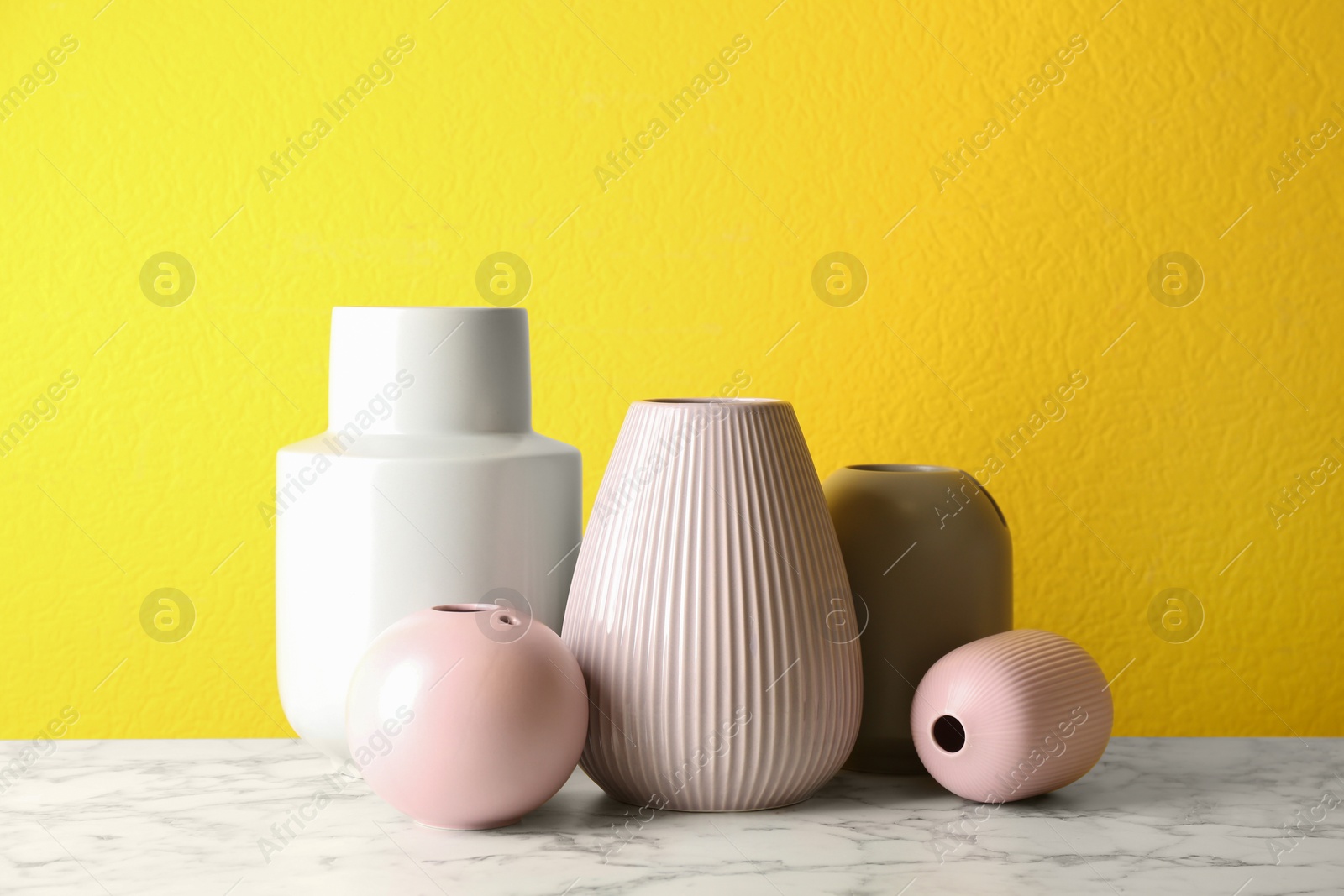 Photo of Stylish ceramic vases on white marble table against yellow background