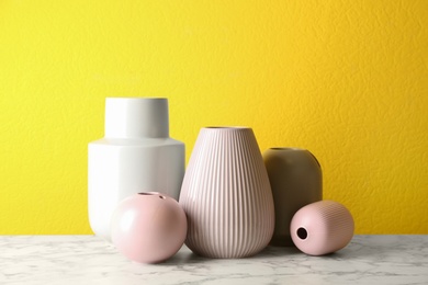 Stylish ceramic vases on white marble table against yellow background