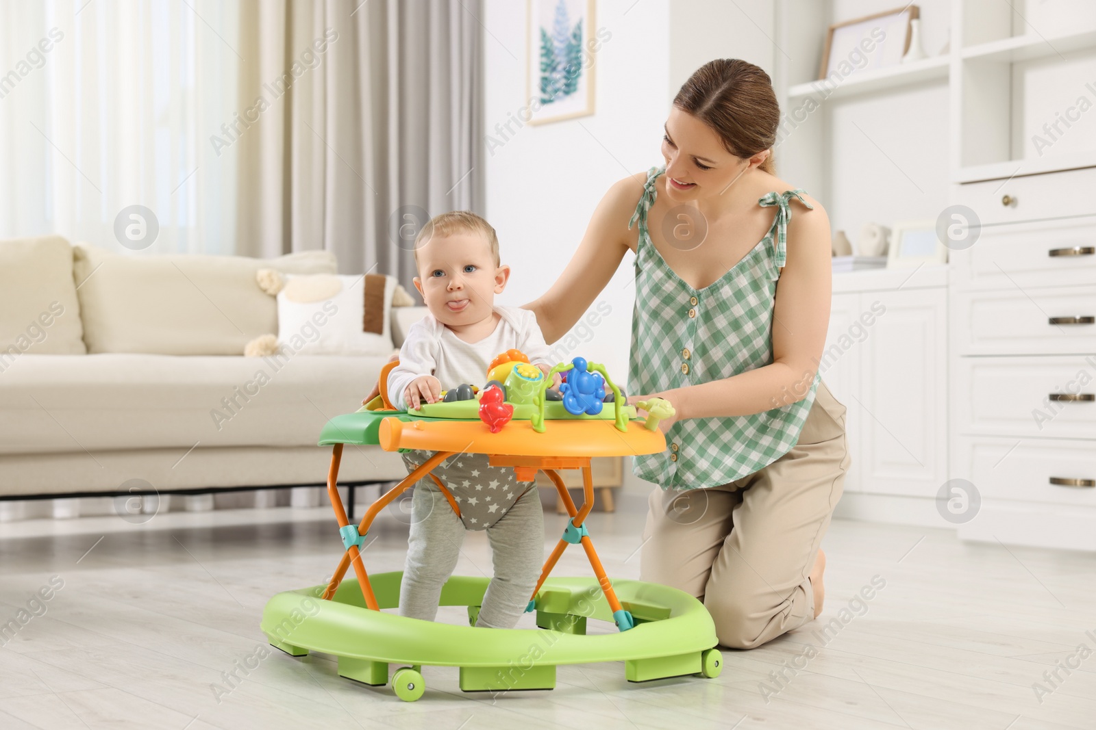 Photo of Cute boy making first steps with baby walker. Happy mother and her little son spending time together at home