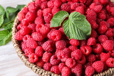 Photo of Tasty ripe raspberries and green leaves on white table, closeup