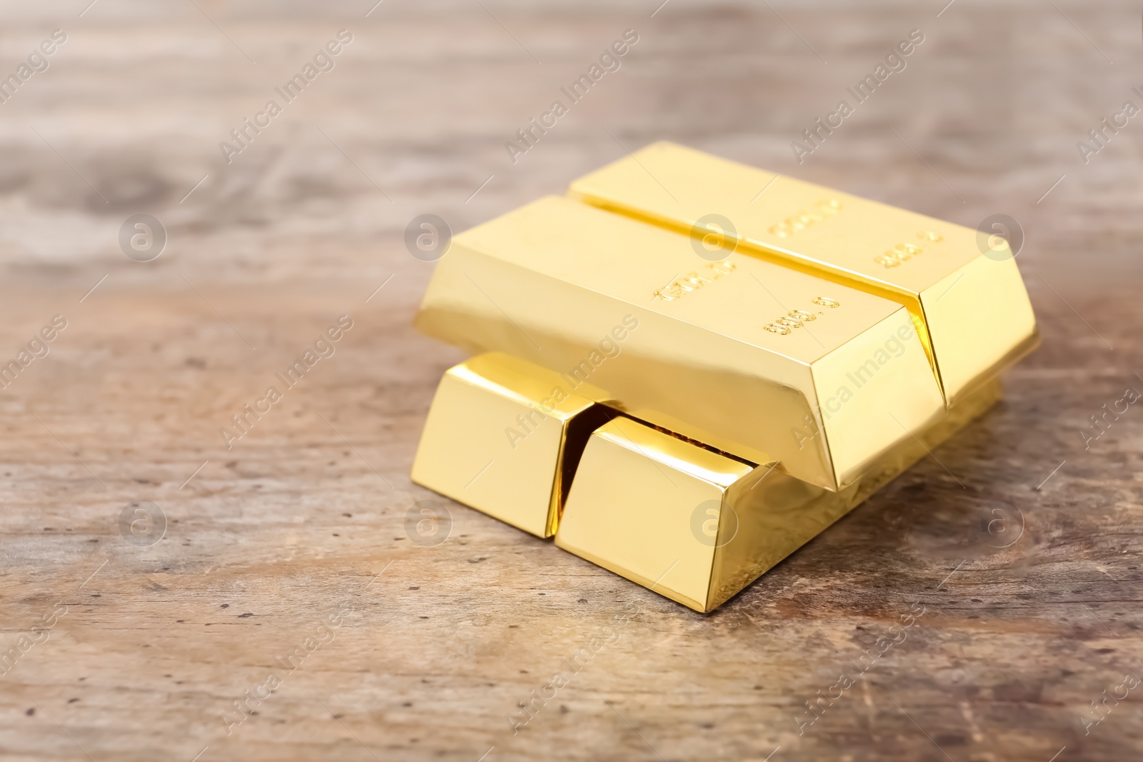 Photo of Stacked shiny gold bars on wooden table. Space for text