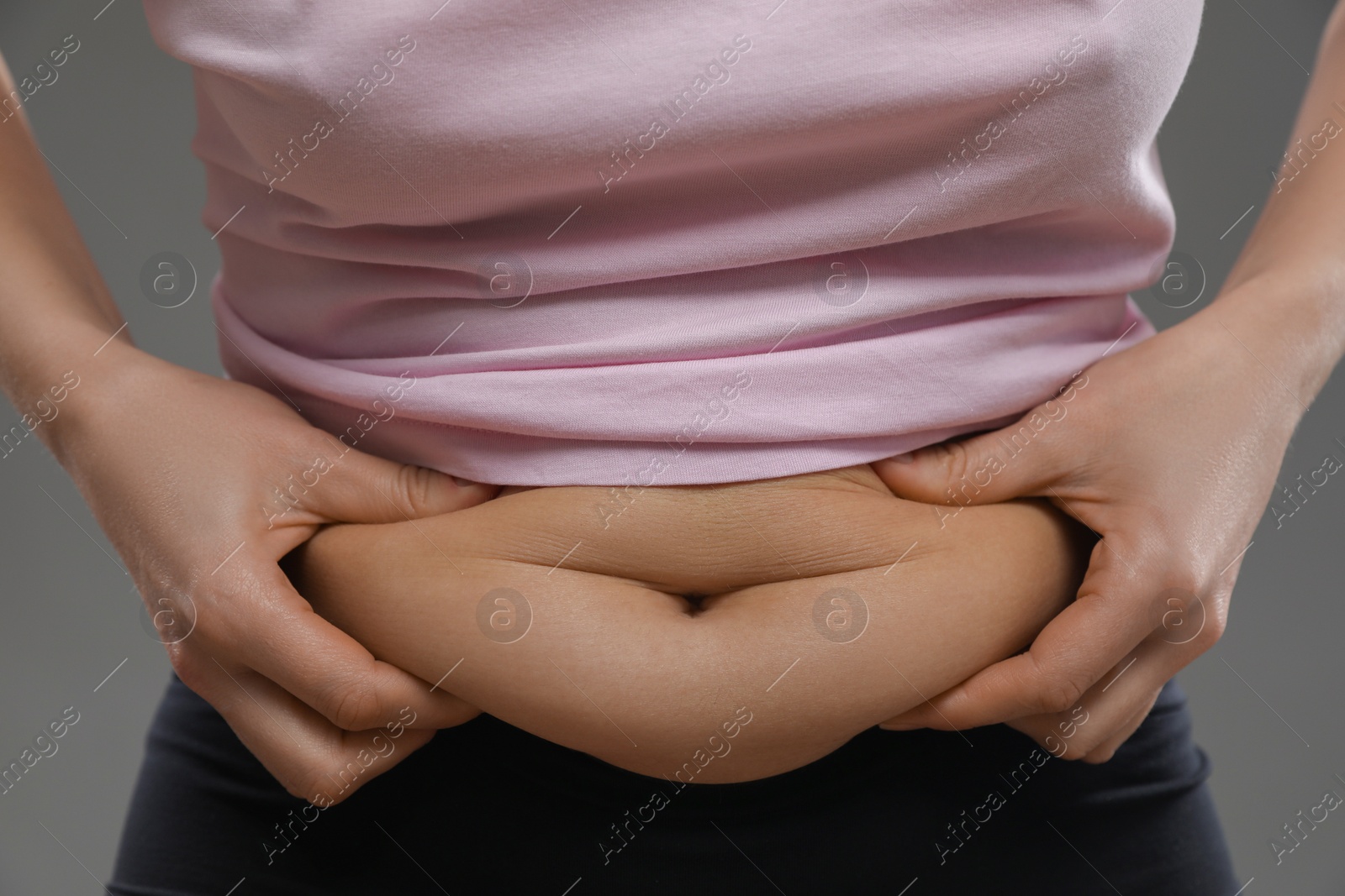 Photo of Woman touching belly fat on grey background, closeup. Overweight problem