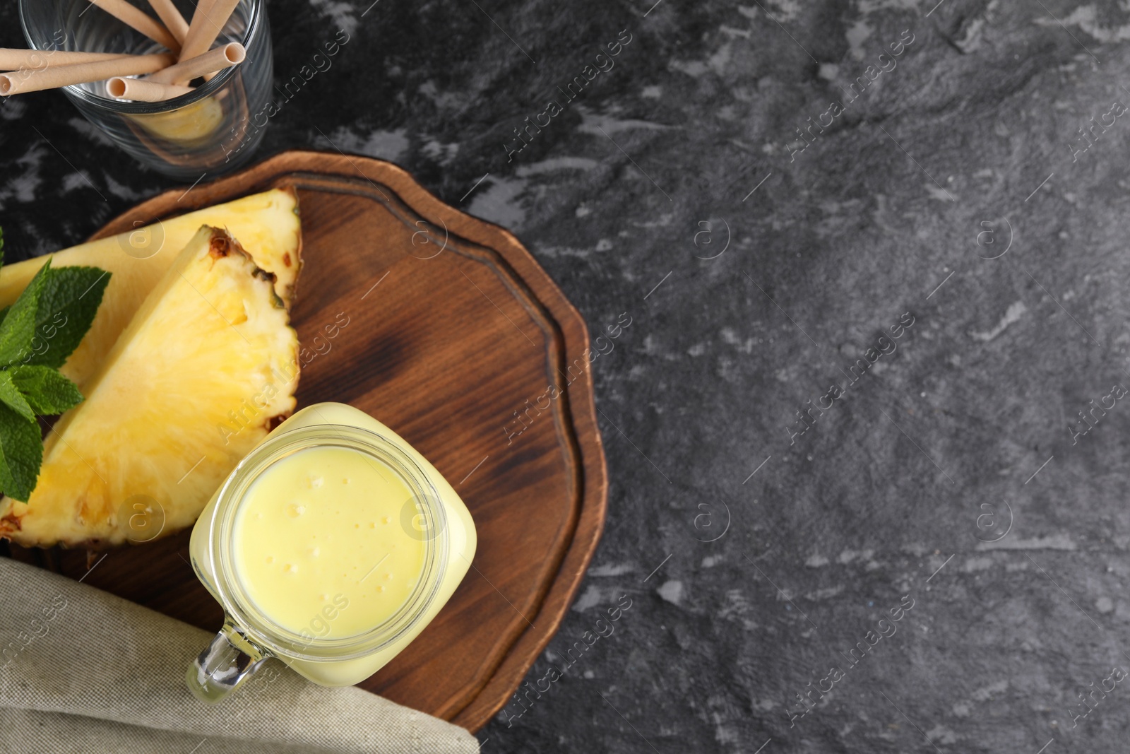 Photo of Tasty pineapple smoothie and straws on dark textured table, flat lay. Space for text