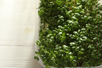 Photo of Sprouted arugula seeds in plastic container on wooden table, top view