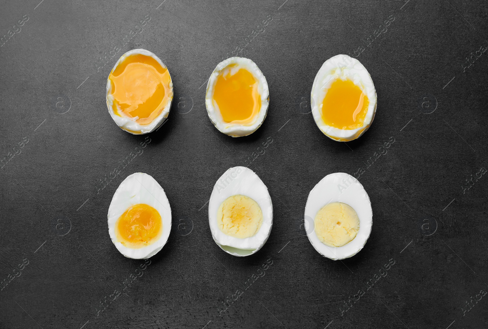 Photo of Different readiness stages of boiled chicken eggs on dark grey table, flat lay