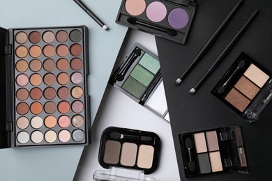 Many different eye shadow palettes and professional makeup brushes on colorful background, flat lay