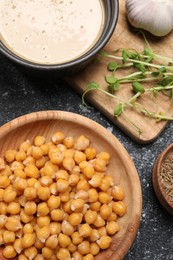 Photo of Delicious chickpeas and different products on black textured table, flat lay. Hummus ingredient