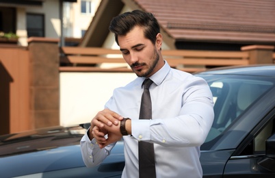 Attractive young man checking time near luxury car outdoors