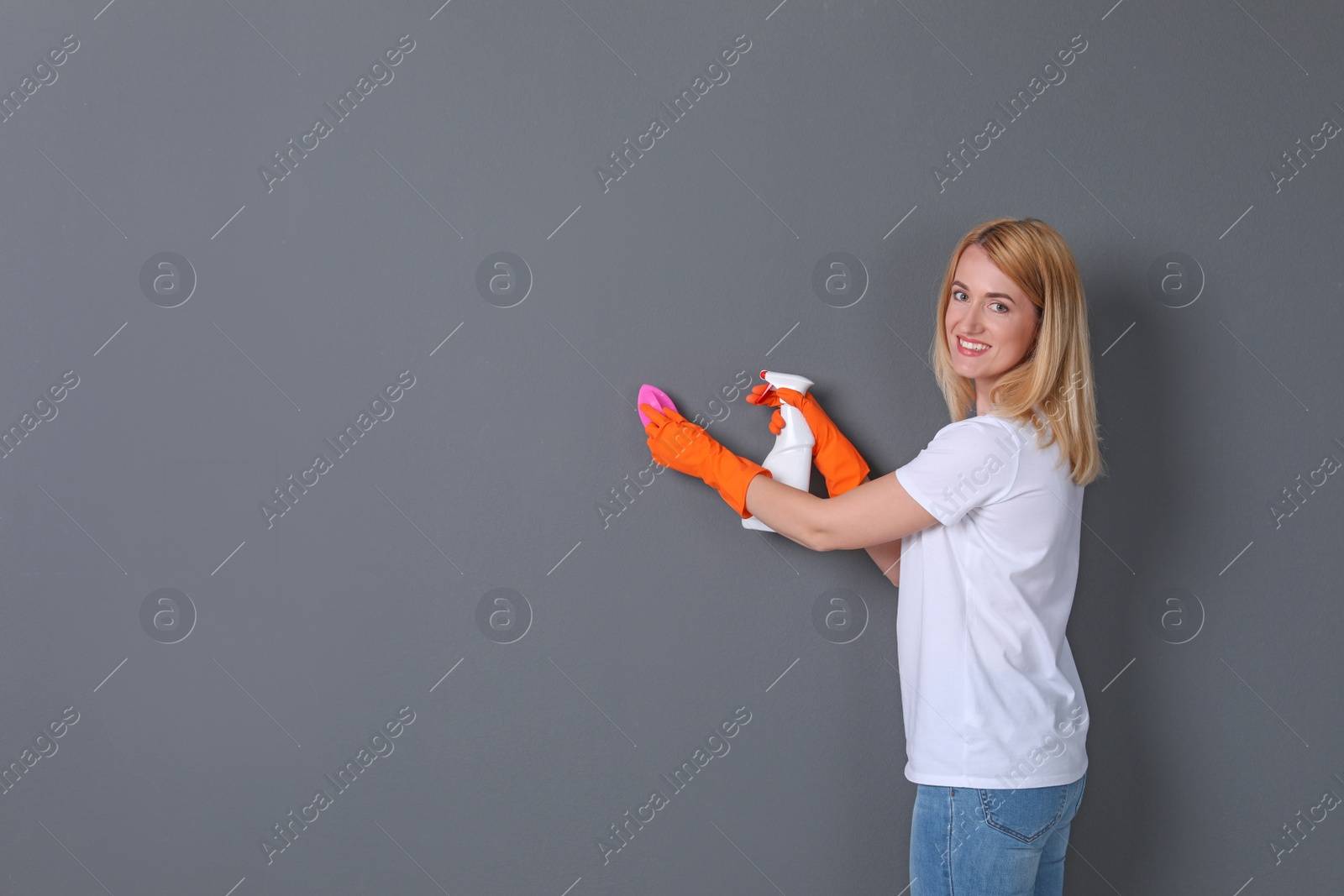 Photo of Woman in gloves cleaning grey wall with brush