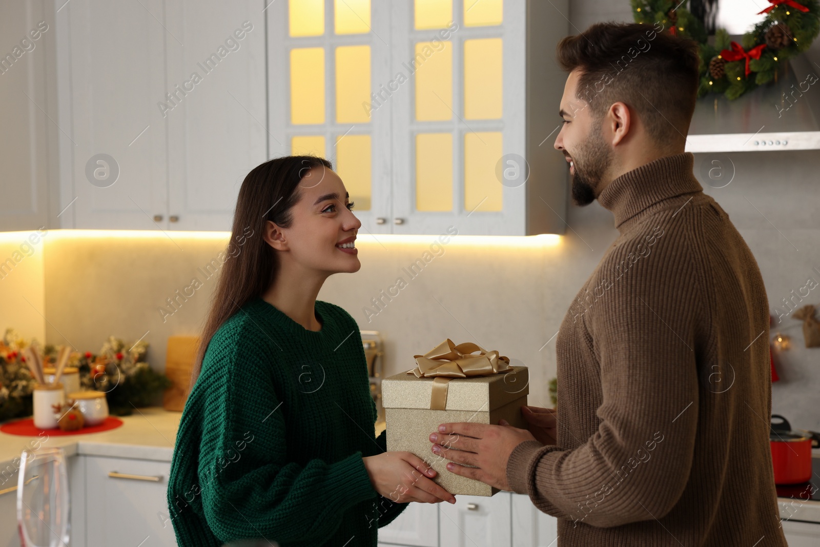 Photo of Happy young man presenting Christmas gift to his girlfriend in kitchen