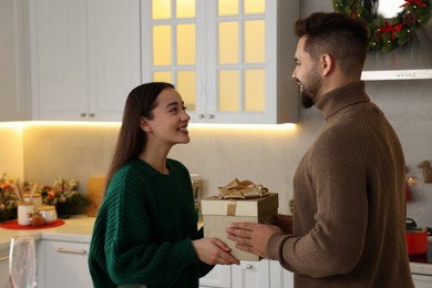 Happy young man presenting Christmas gift to his girlfriend in kitchen