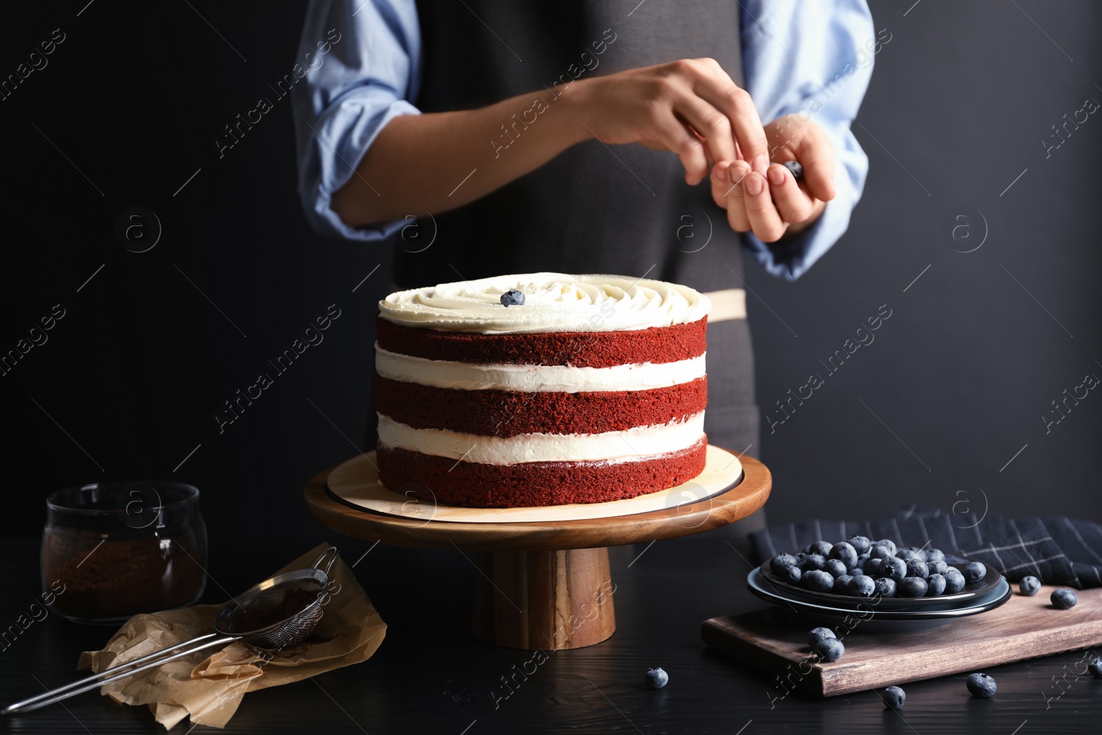 Photo of Woman decorating delicious homemade red velvet cake with blueberries at table