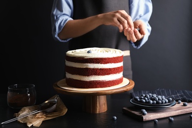 Photo of Woman decorating delicious homemade red velvet cake with blueberries at table