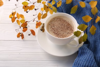 Photo of Cup of hot drink, leaves and knitted sweater on white wooden table. Cozy autumn atmosphere