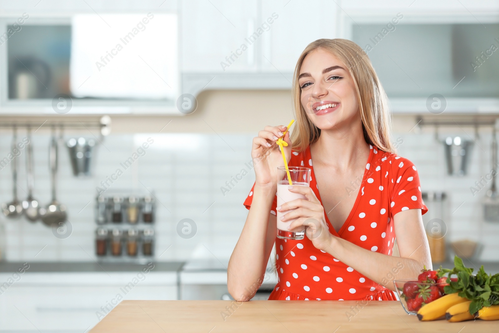 Photo of Young woman with glass of delicious milk shake in kitchen