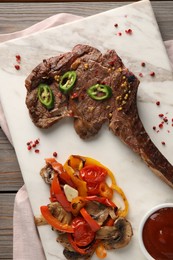 Delicious fried beef meat served with vegetables and sauce on wooden table, top view