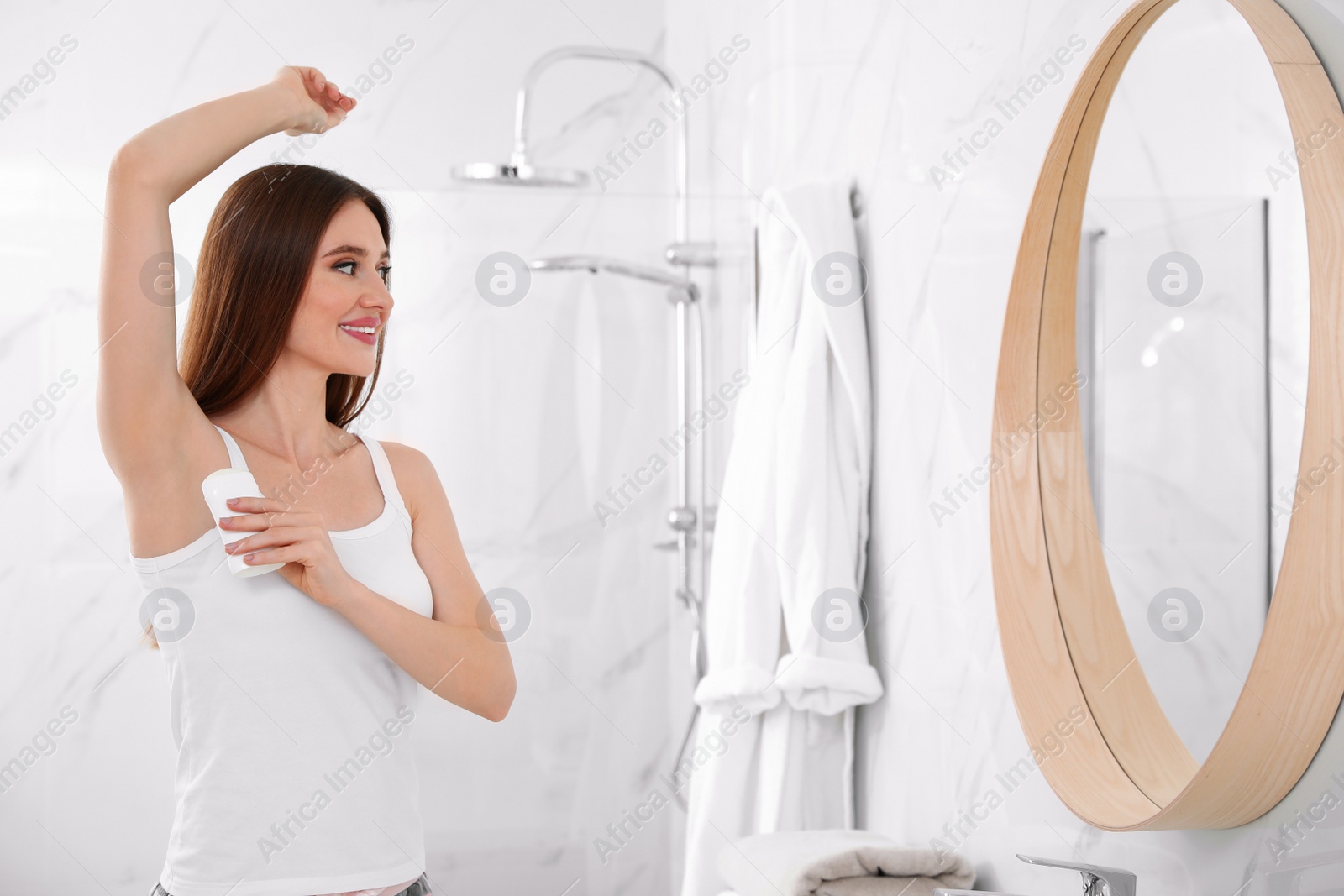 Photo of Beautiful young woman applying deodorant in bathroom