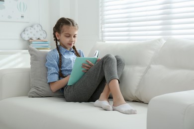 Photo of Cute little girl reading book on sofa at home