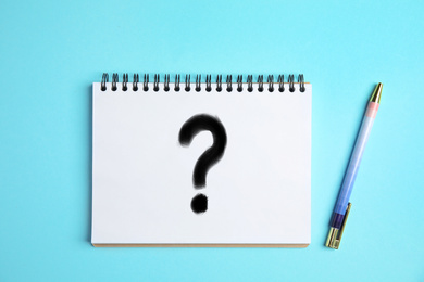 Image of Notebook with question mark and pen on light blue background, top view