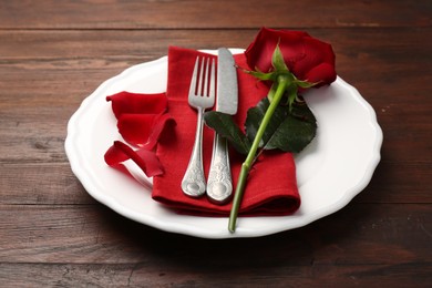 Photo of Romantic place setting with red rose on wooden table. St. Valentine's day dinner