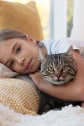 Cute little girl with her cat at home, closeup. Childhood pet