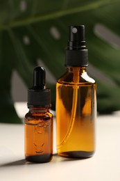 Photo of Bottles with oil and green leaf on white table. Natural cosmetics