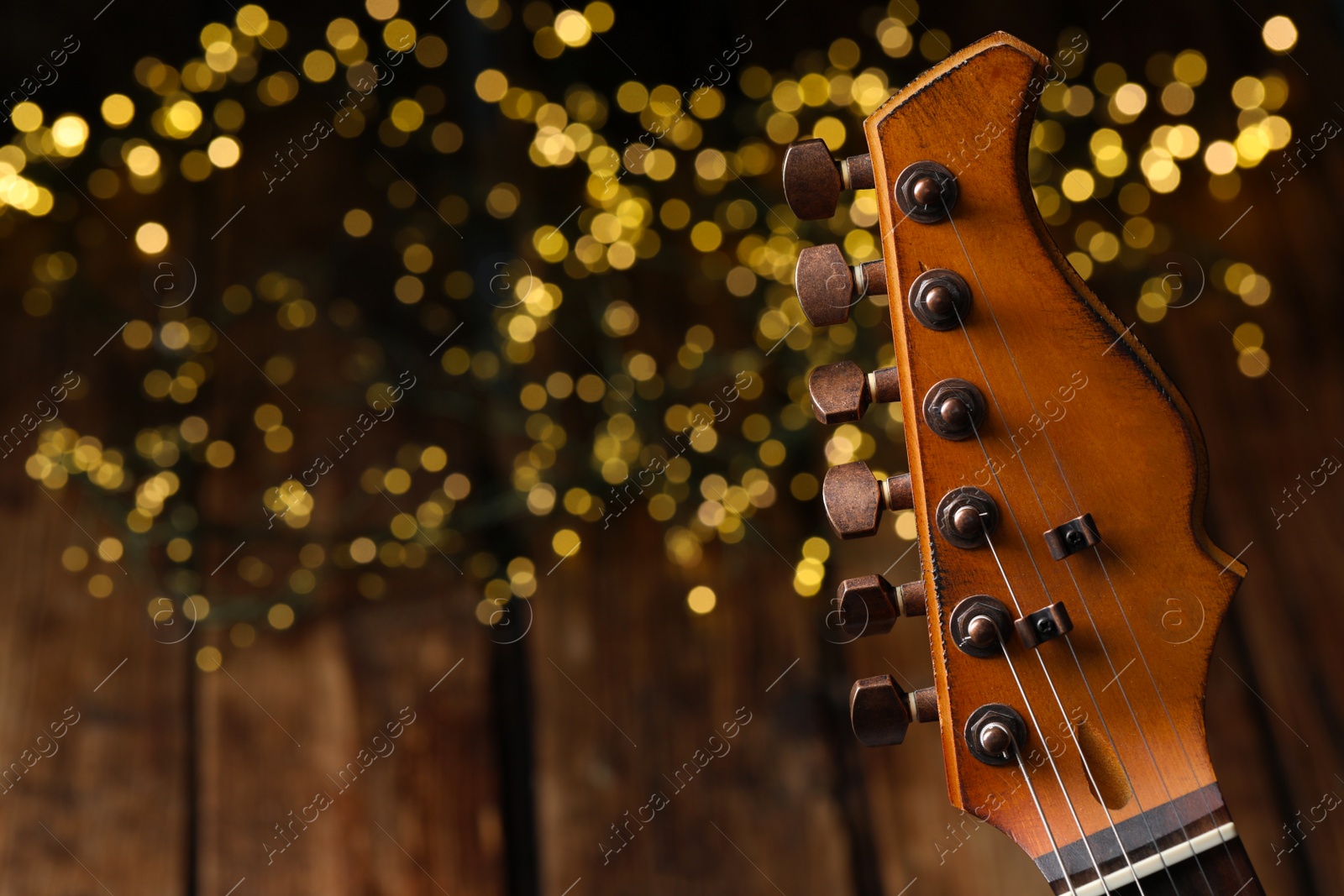 Photo of Closeup view of guitar at wooden table against blurred lights, space for text