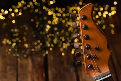 Photo of Closeup view of guitar at wooden table against blurred lights, space for text
