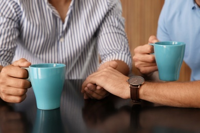 Happy gay couple with coffee at table indoors, closeup