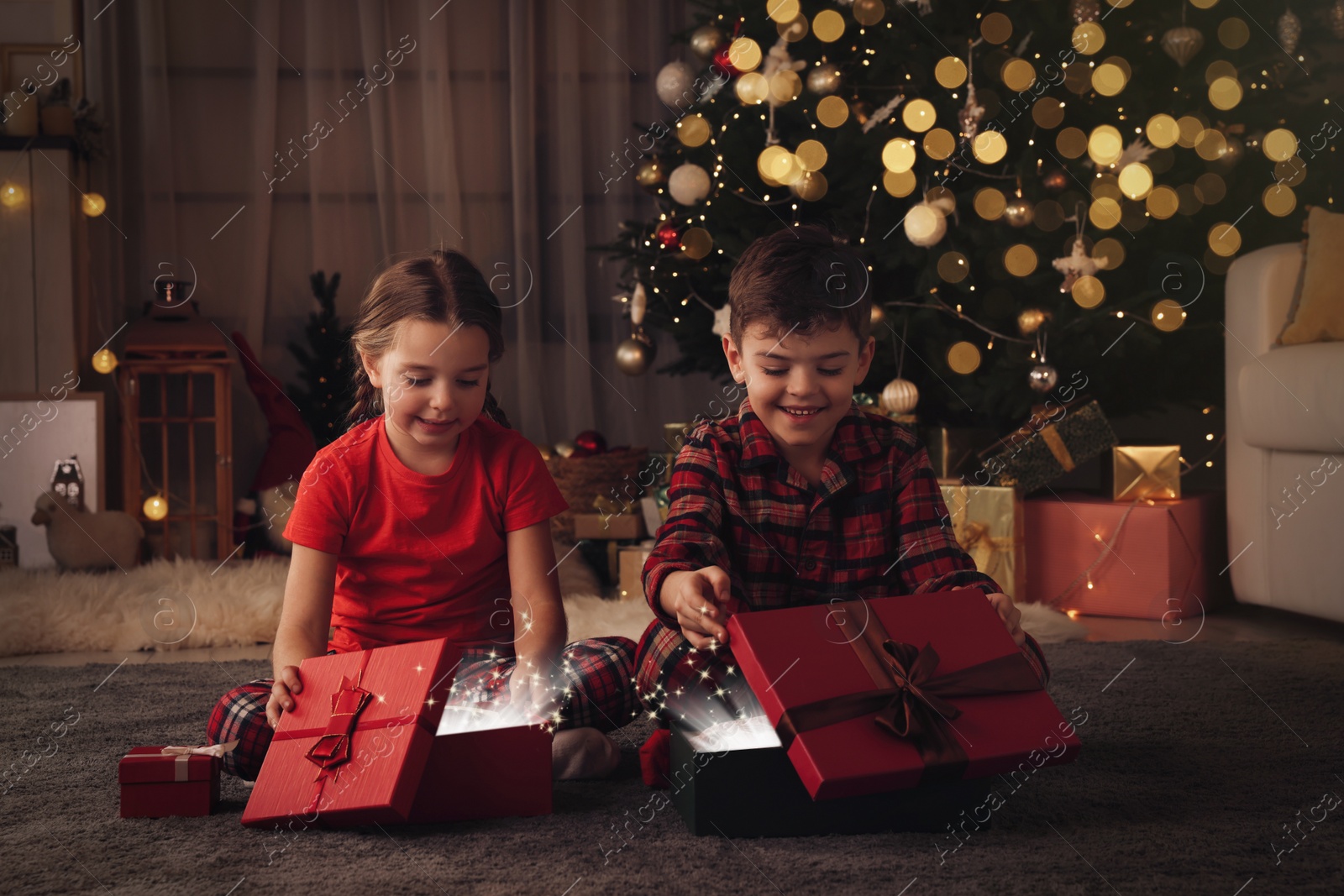 Photo of Cute little children with gift boxes near Christmas tree at home