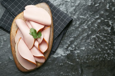 Photo of Board with slices of tasty boiled sausage and parsley on dark textured table, top view. Space for text