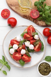 Photo of Delicious Caprese sandwiches with mozzarella, tomatoes, basil and pesto sauce on white wooden table, flat lay